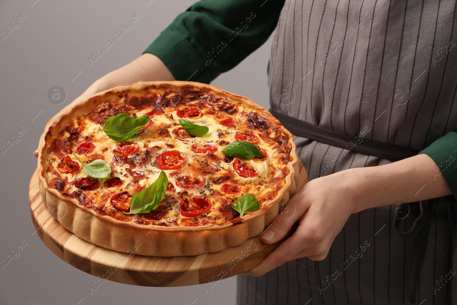 Photo of Woman holding delicious homemade quiche with prosciutto on light grey background, closeup