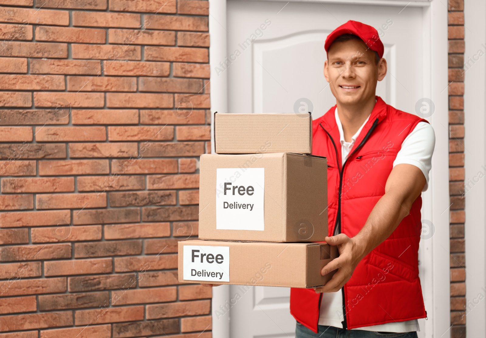 Photo of Courier holding parcels with stickers Free Delivery indoors