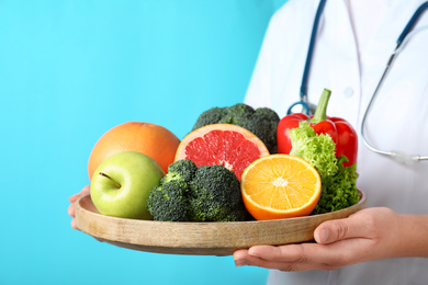 Photo of Female nutritionist with fruits and vegetables on light blue background, closeup