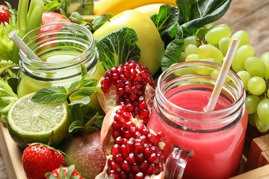 Photo of Mason jars with juices and fresh fruits in wooden crate