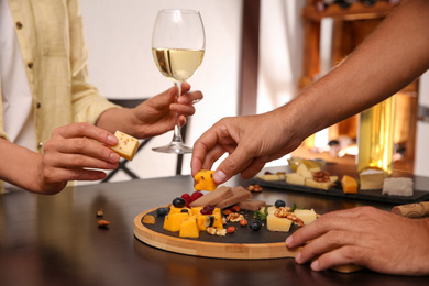 Couple with different types of delicious cheeses at table indoors, closeup