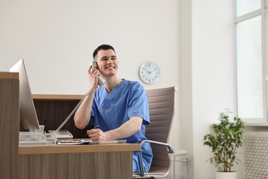Photo of Smiling medical assistant talking by phone at hospital reception. Space for text