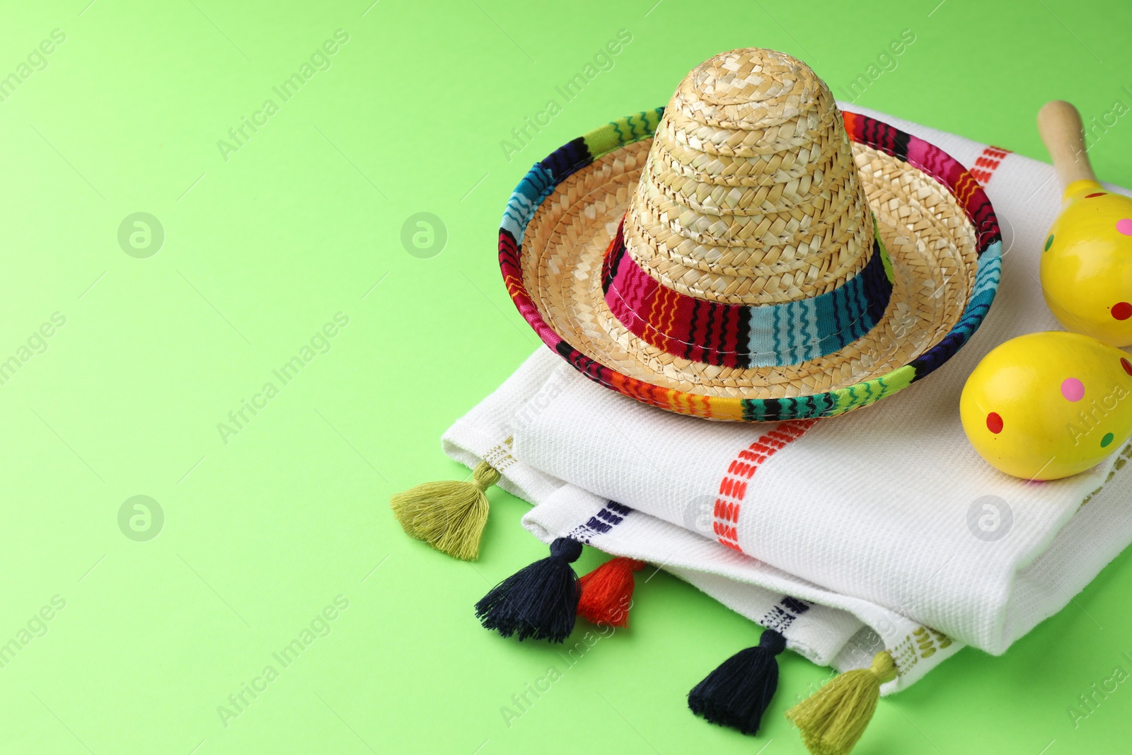 Photo of Mexican sombrero hat, maracas and poncho on green background. Space for text