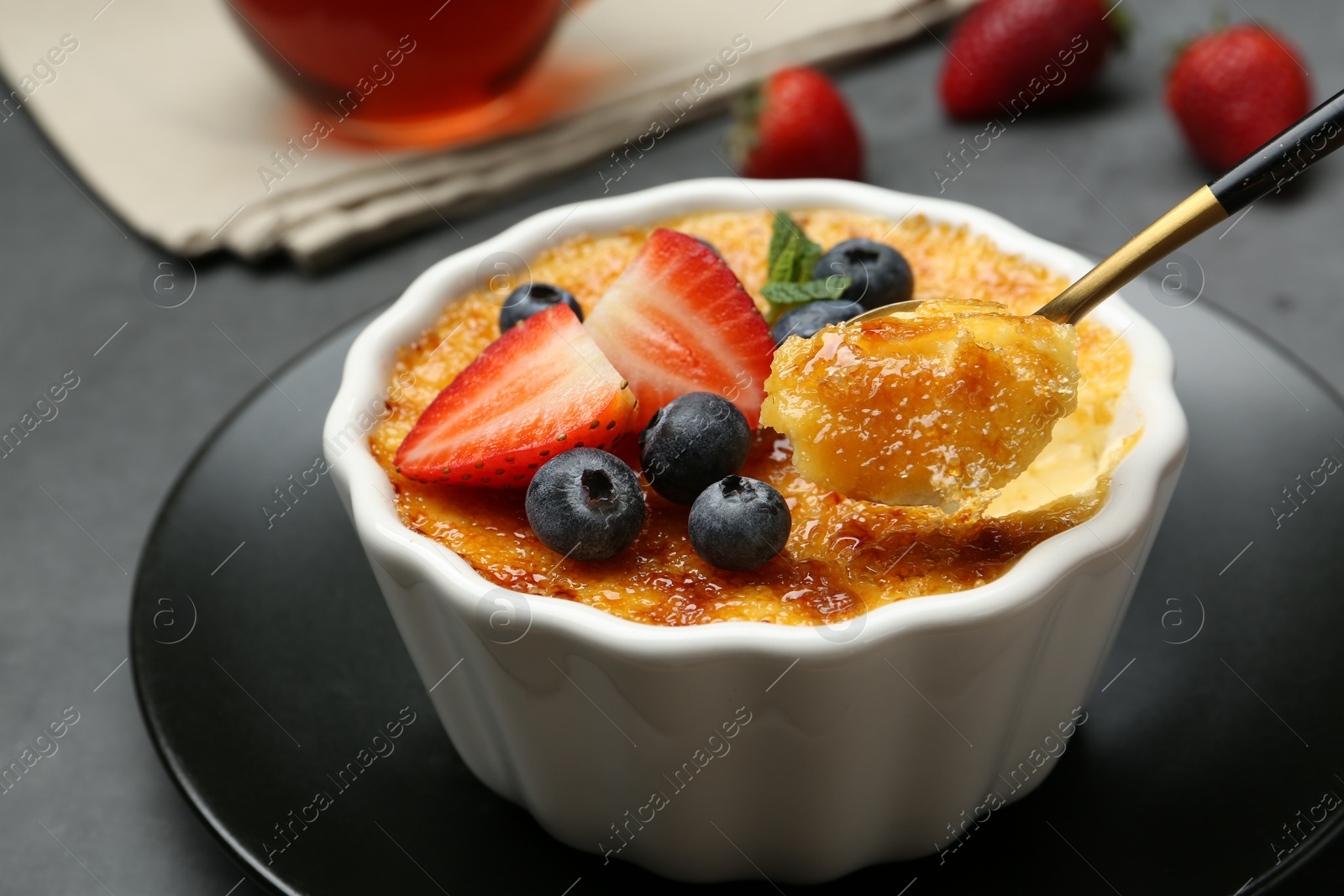 Photo of Taking delicious creme brulee with berries from bowl at grey table, closeup