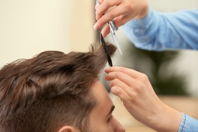 Photo of Barber making stylish haircut with professional scissors in beauty salon, closeup