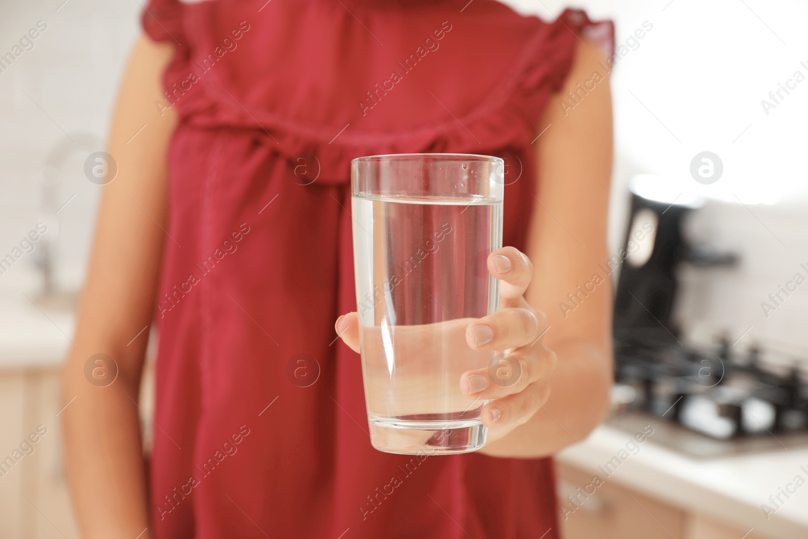 Photo of Woman holding glass with pure water in kitchen, closeup