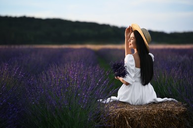Photo of Woman sitting on hay bale in lavender field, back view
