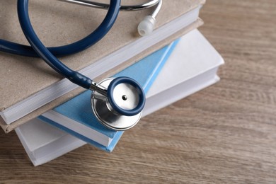 Photo of Student textbooks and stethoscope on wooden table, closeup view with space for text Medical education