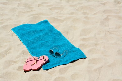 Photo of Soft blue beach towel, pink flip flops and sunglasses on sand. Space for text