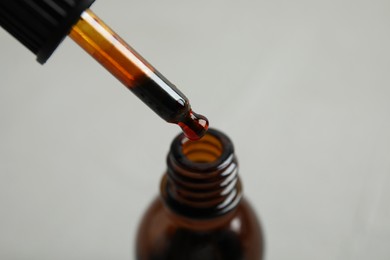 Photo of Dripping medical iodine from pipette into glass bottle on grey background, closeup