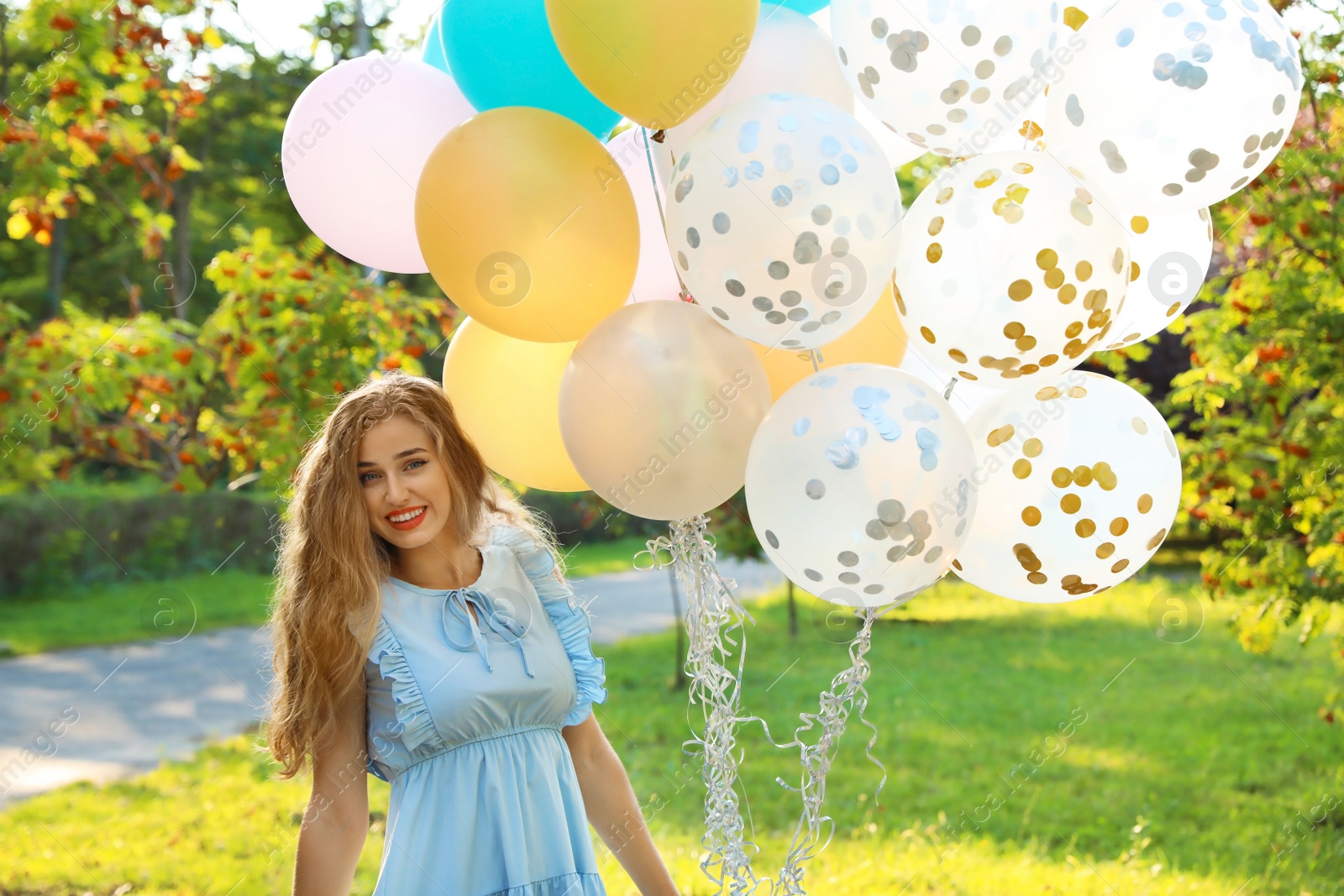 Photo of Beautiful young woman holding colorful balloons in park