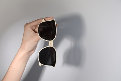 Photo of Woman holding stylish sunglasses on light background, closeup. Space for text