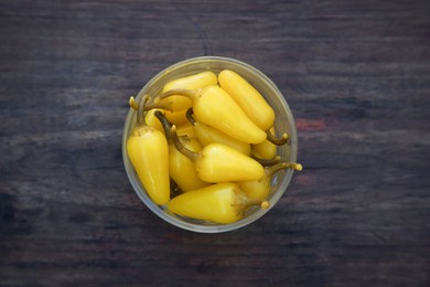 Photo of Bowl of pickled yellow jalapeno peppers on wooden table, top view