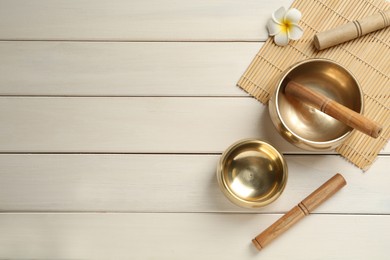 Flat lay composition with golden singing bowls on white wooden table. Space for text