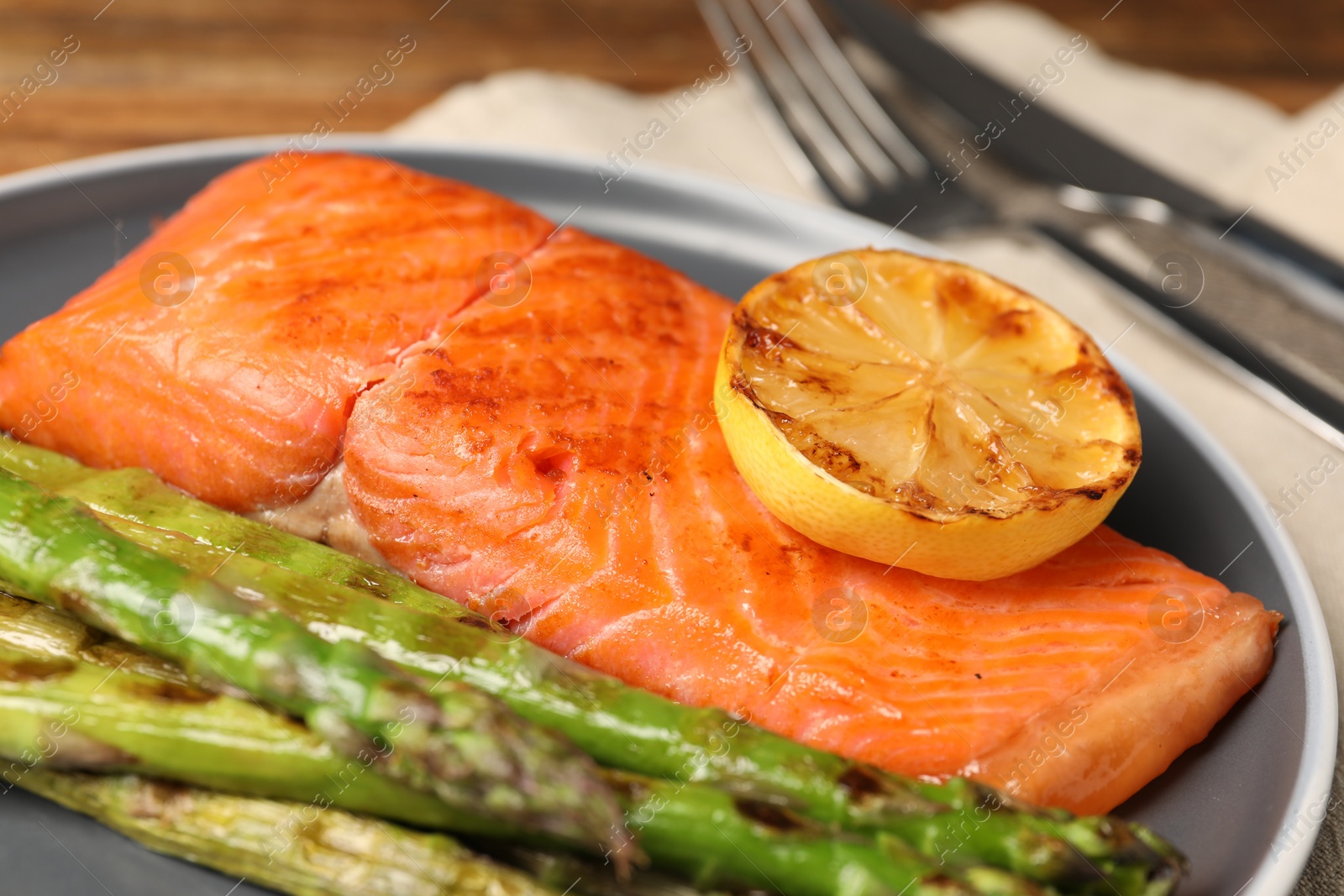 Photo of Tasty grilled salmon with asparagus and lemon served on plate, closeup