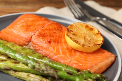 Photo of Tasty grilled salmon with asparagus and lemon served on plate, closeup