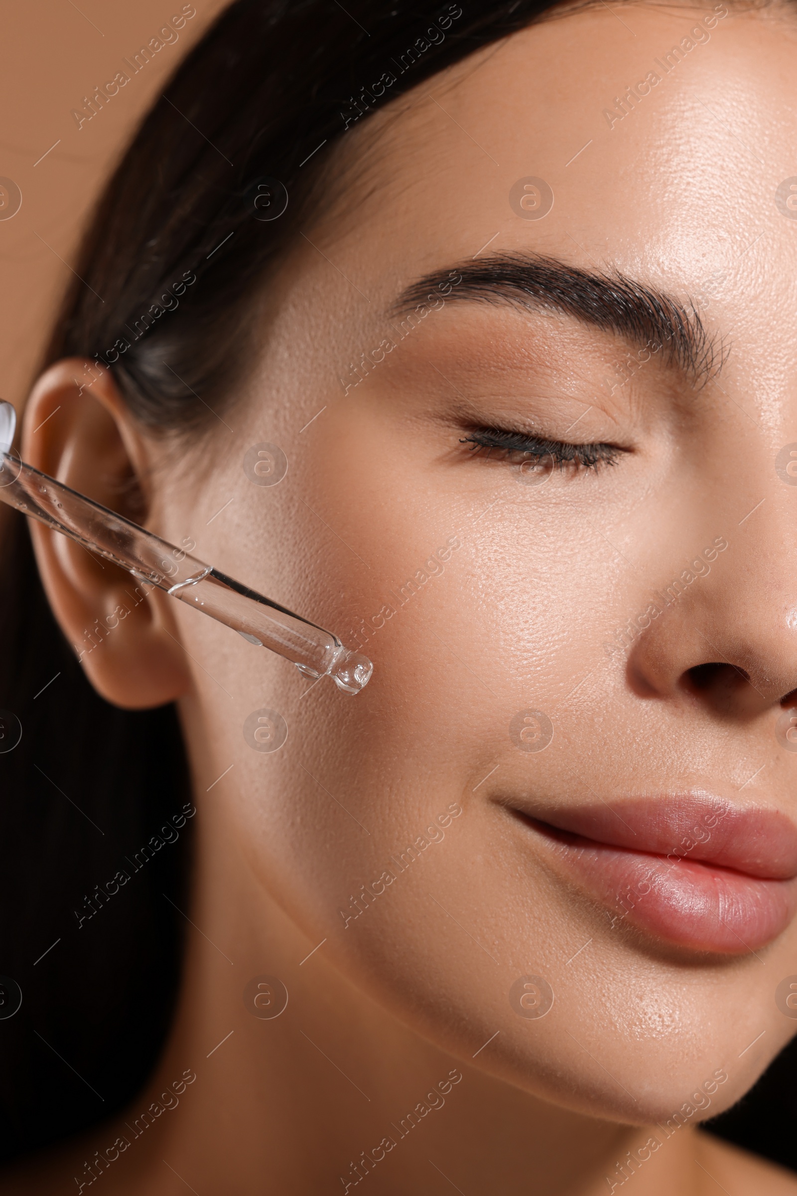 Photo of Beautiful young woman applying serum onto her face, closeup