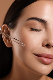 Photo of Beautiful young woman applying serum onto her face, closeup