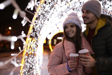 Young couple with cups of mulled wine at winter fair. Space for text