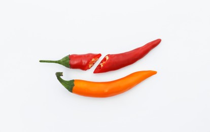 Photo of Cut and whole hot chili peppers on white background, flat lay