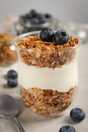 Glass of yogurt with granola and blueberries on grey marble table, closeup