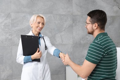 Doctor shaking hands with patient after consultation near grey wall