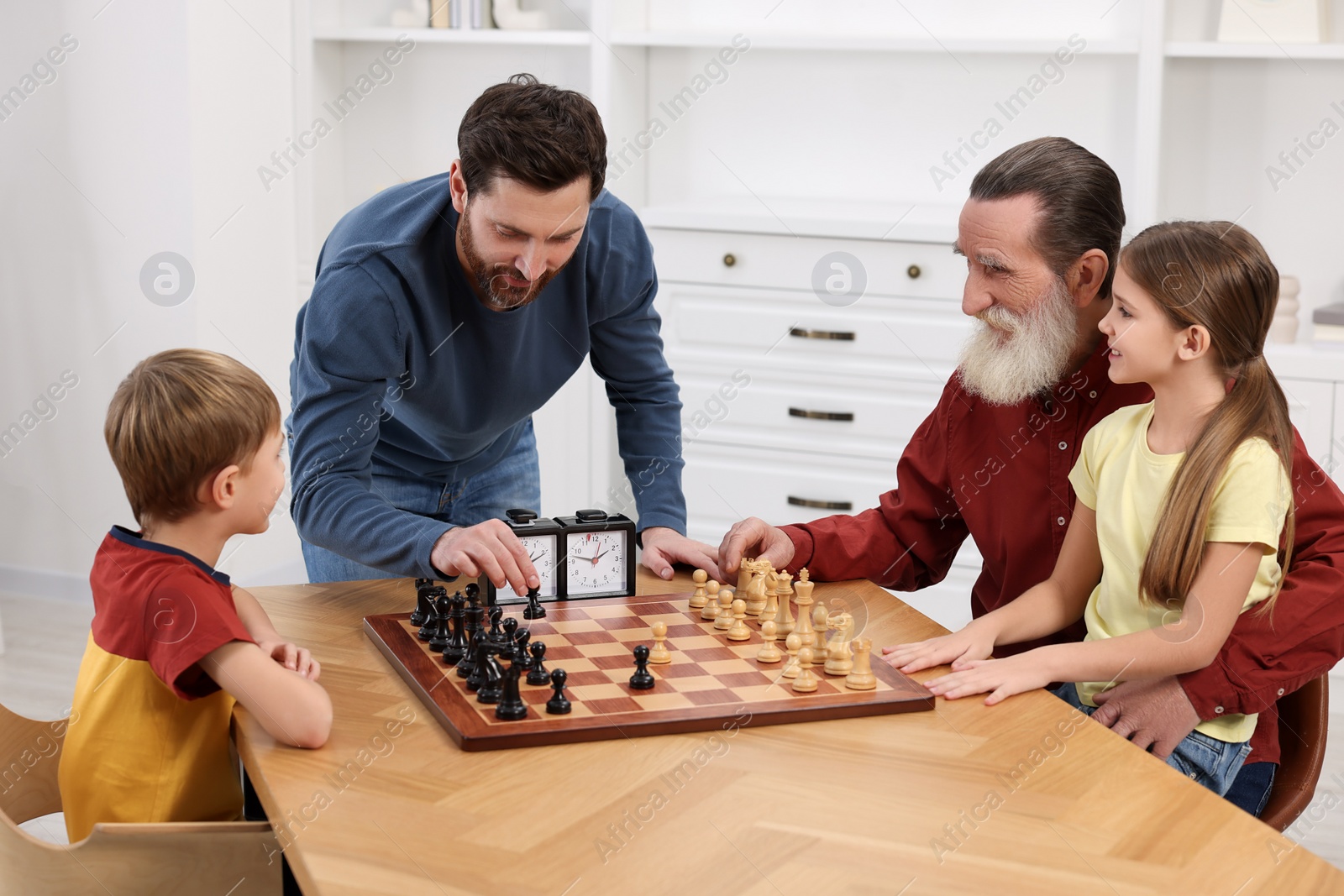 Photo of Family playing chess together at table in room