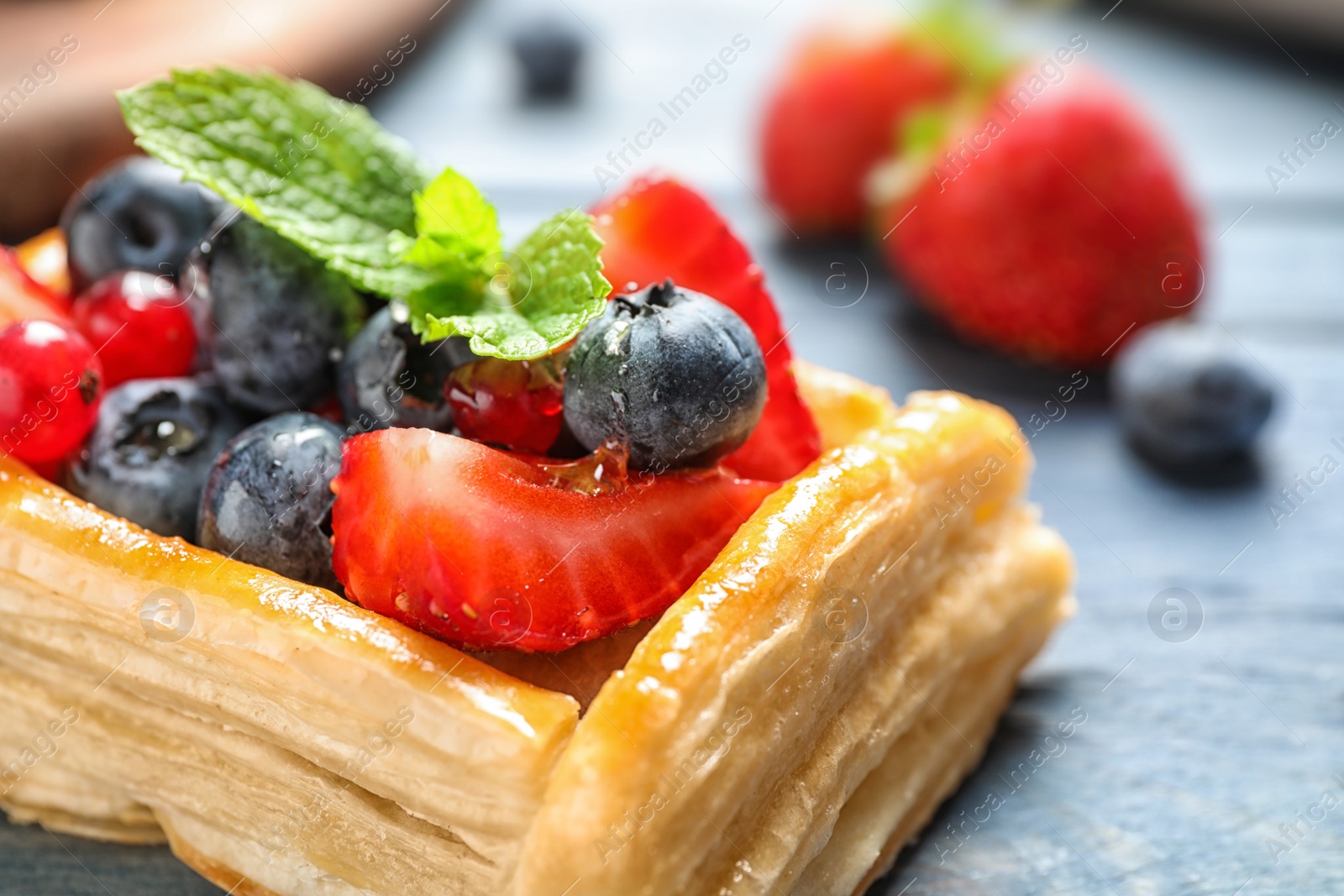 Photo of Fresh delicious puff pastry with sweet berries on blue wooden table, closeup