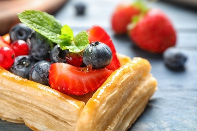 Fresh delicious puff pastry with sweet berries on blue wooden table, closeup