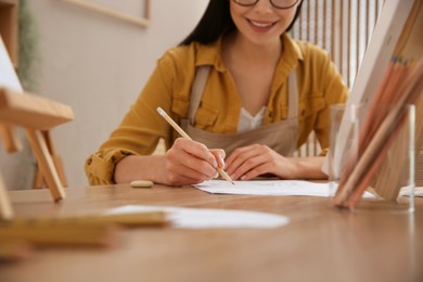 Photo of Young woman drawing with pencil at table indoors, closeup