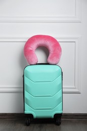 Photo of Pink travel pillow on turquoise suitcase near white wall indoors