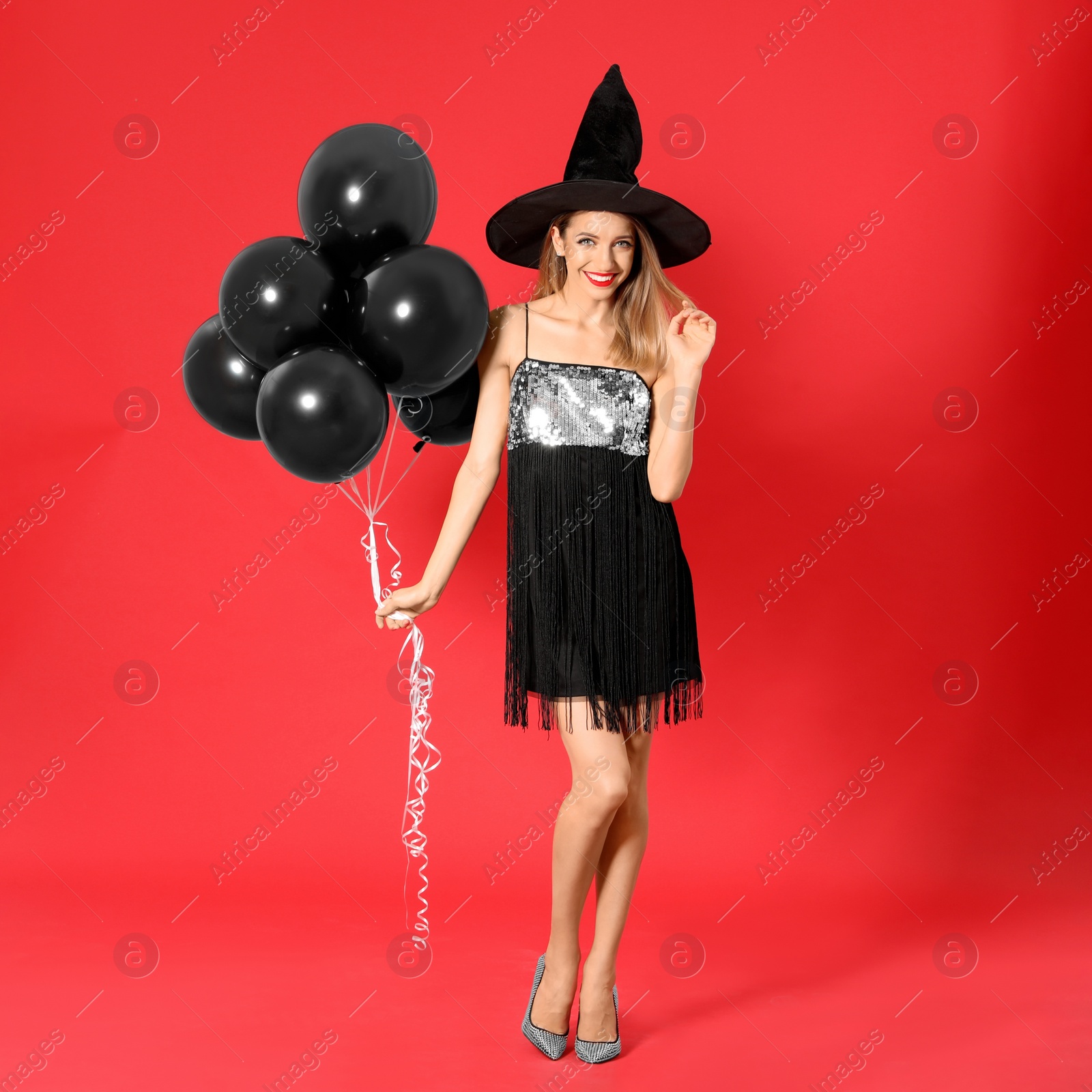 Photo of Beautiful woman wearing witch costume with balloons for Halloween party on red background