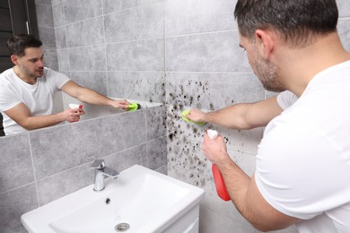 Image of Man using mold remover and brush on wall in bathroom