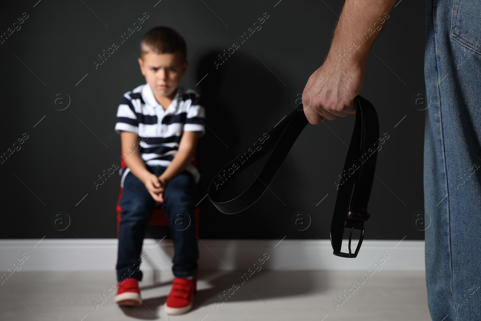 Photo of Man threatening his son with belt indoors, closeup. Domestic violence concept