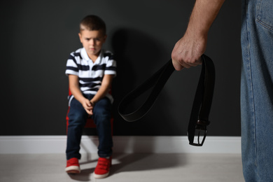 Photo of Man threatening his son with belt indoors, closeup. Domestic violence concept