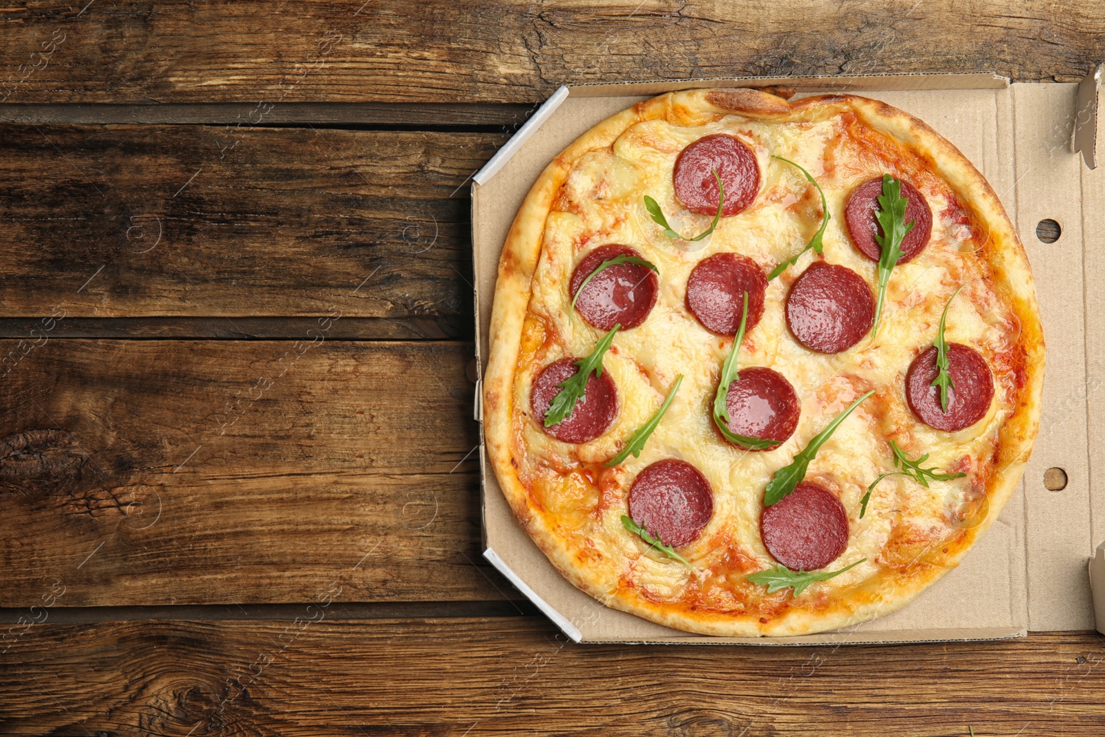 Photo of Tasty pepperoni pizza in cardboard box on wooden table, top view. Space for text