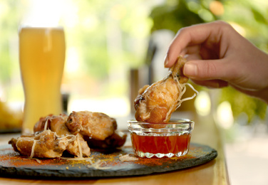 Photo of Woman dipping tasty BBQ wing into sauce at table, closeup