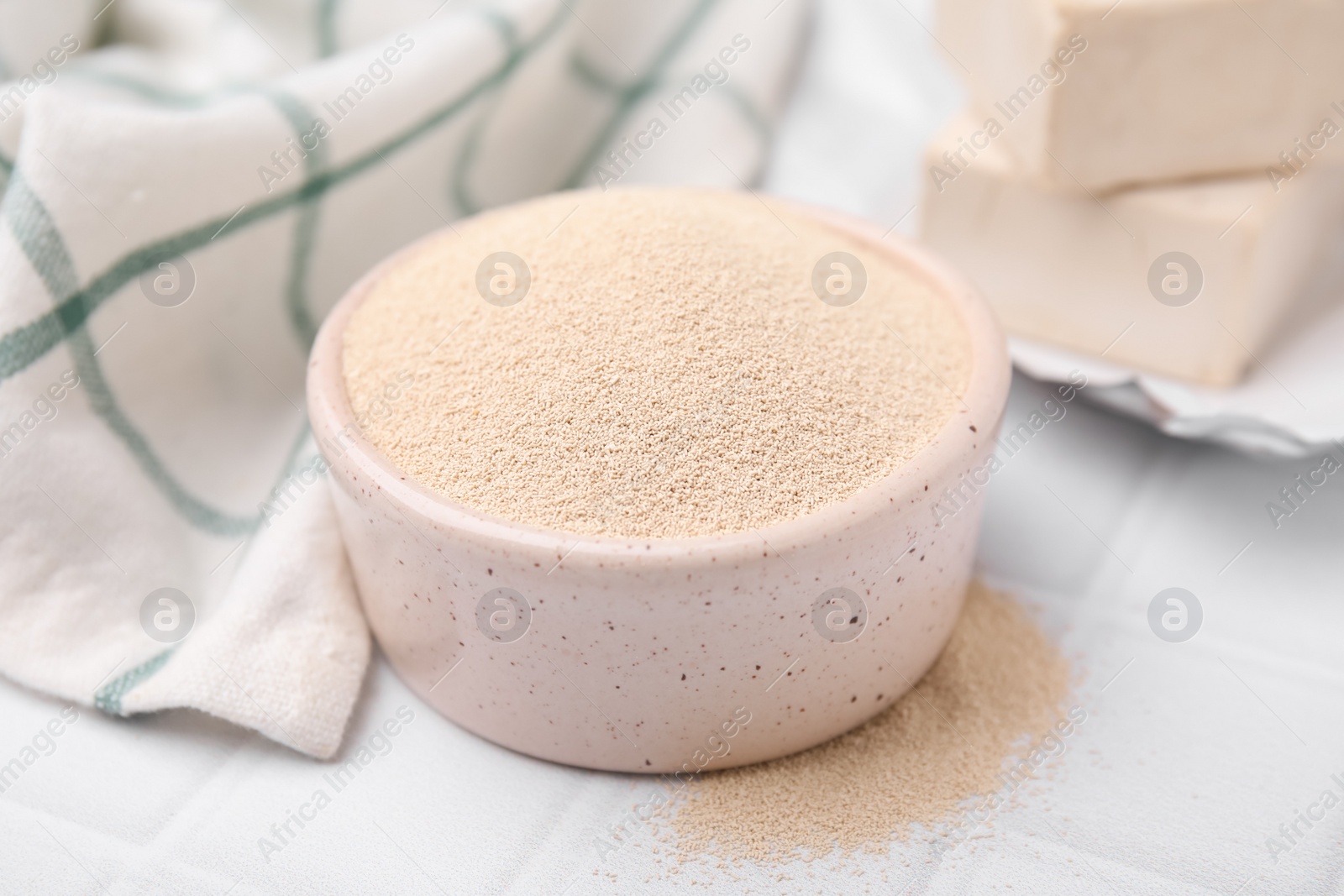 Photo of Granulated yeast in bowl on white tiled table, closeup