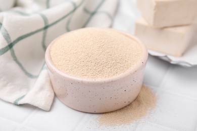 Granulated yeast in bowl on white tiled table, closeup