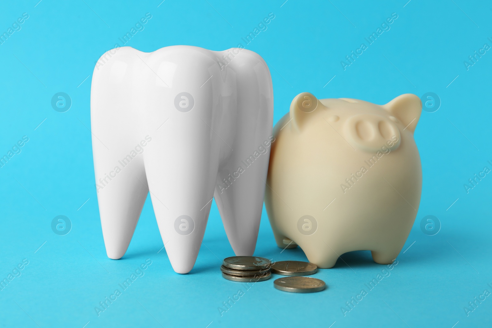 Photo of Ceramic model of tooth, piggy bank and coins on light blue background. Expensive treatment