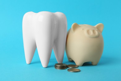 Photo of Ceramic model of tooth, piggy bank and coins on light blue background. Expensive treatment