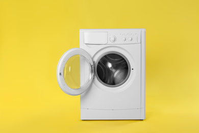 Photo of Modern washing machine on yellow background. Laundry day