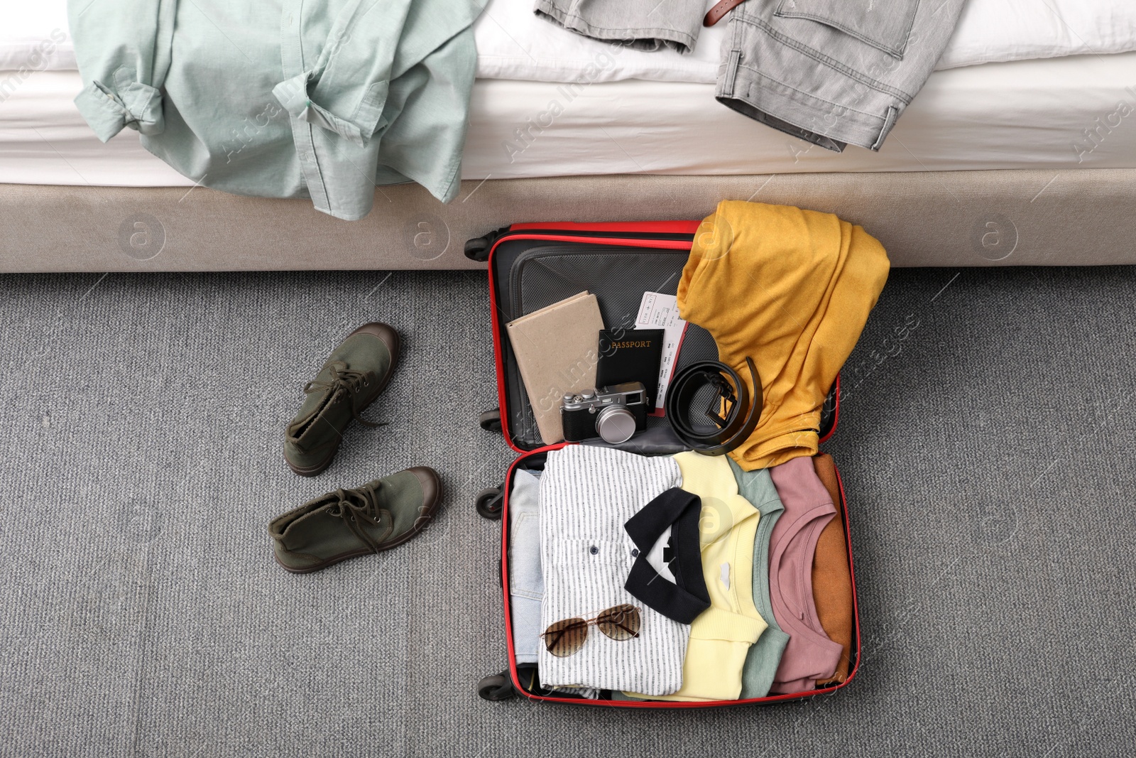 Photo of Open suitcase with clothes, accessories and shoes on floor near bed indoors, flat lay