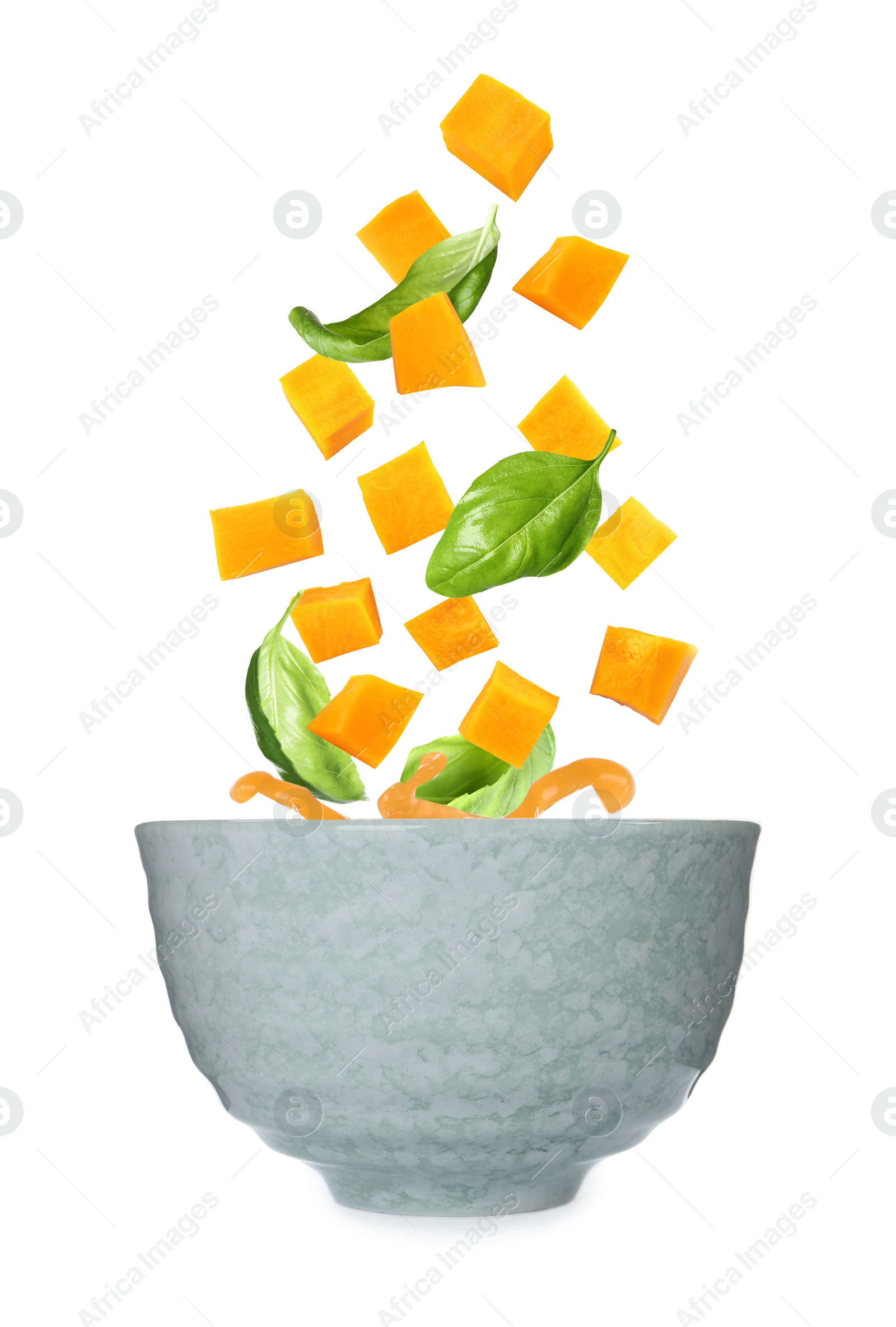 Image of Ingredients falling into bowl of homemade pumpkin soup on white background 