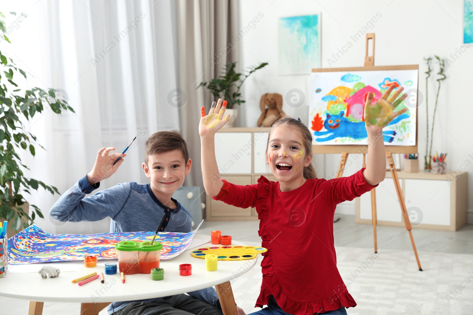 Photo of Happy children having fun with paints together at table indoors