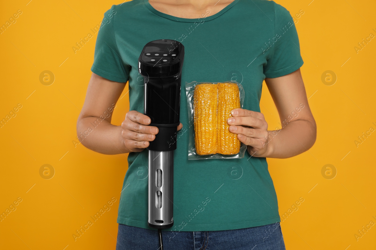 Photo of Woman holding sous vide cooker and corn in vacuum pack on orange background, closeup