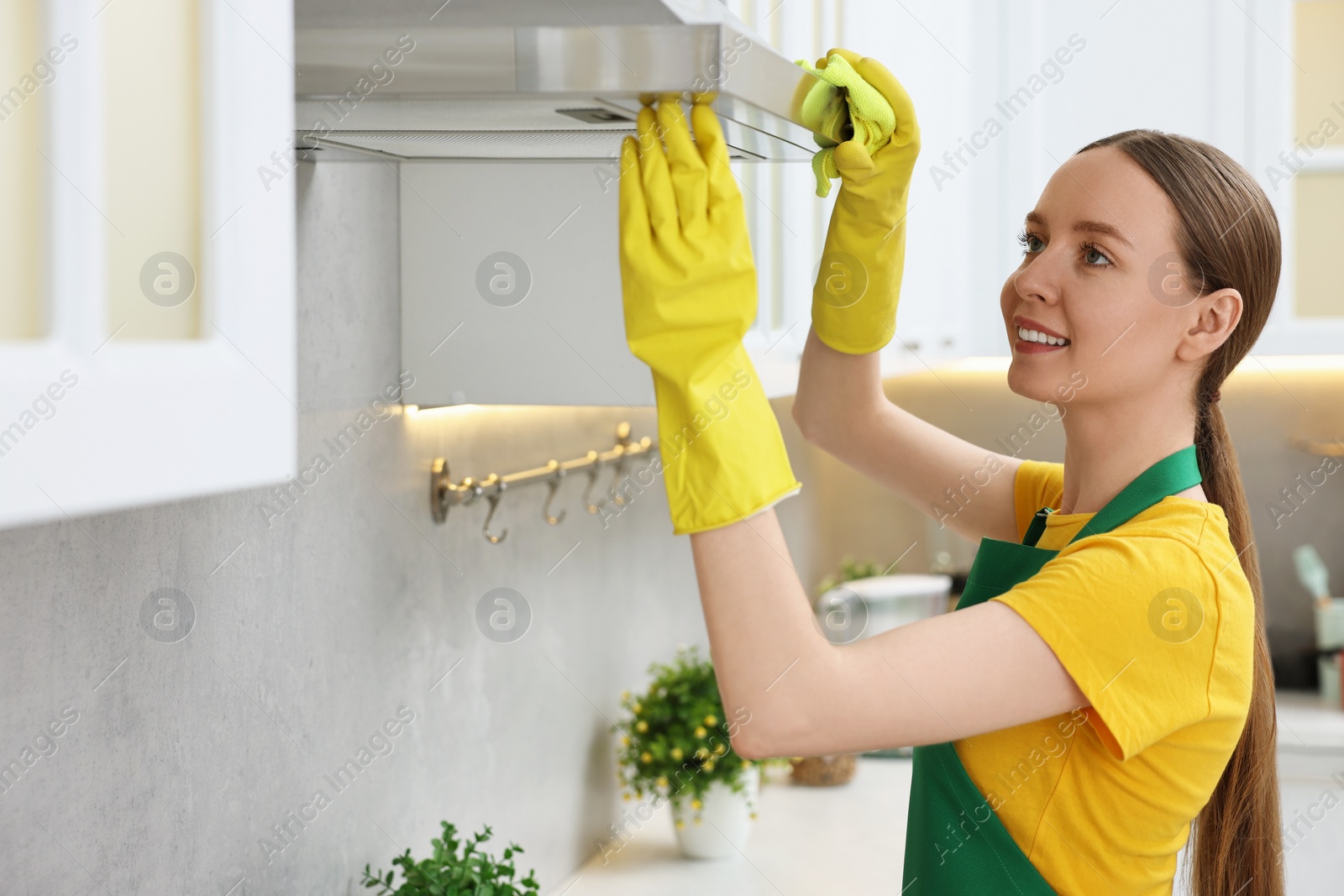 Photo of Woman cleaning kitchen hood with rag indoors