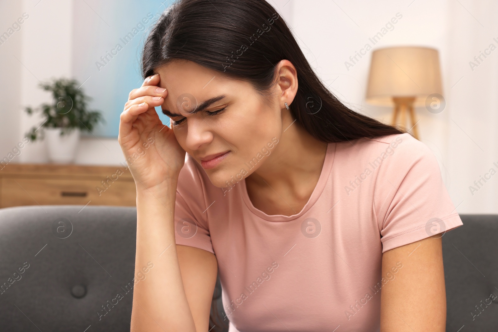 Photo of Sad woman suffering from headache on sofa indoors