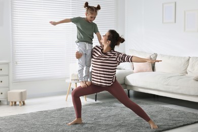 Young mother and her daughter practicing yoga together at home