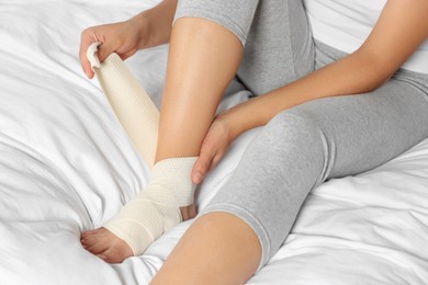 Young woman applying medical bandage onto foot on bed, closeup